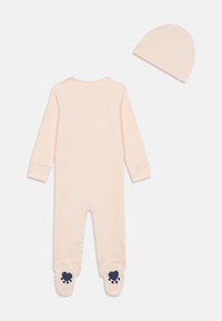 Body rosa chiaro per neonati con maniche lunghe, caratterizzato da cuori blu navy e impronte di zampe sulle suole, accompagnato da un berretto abbinato.