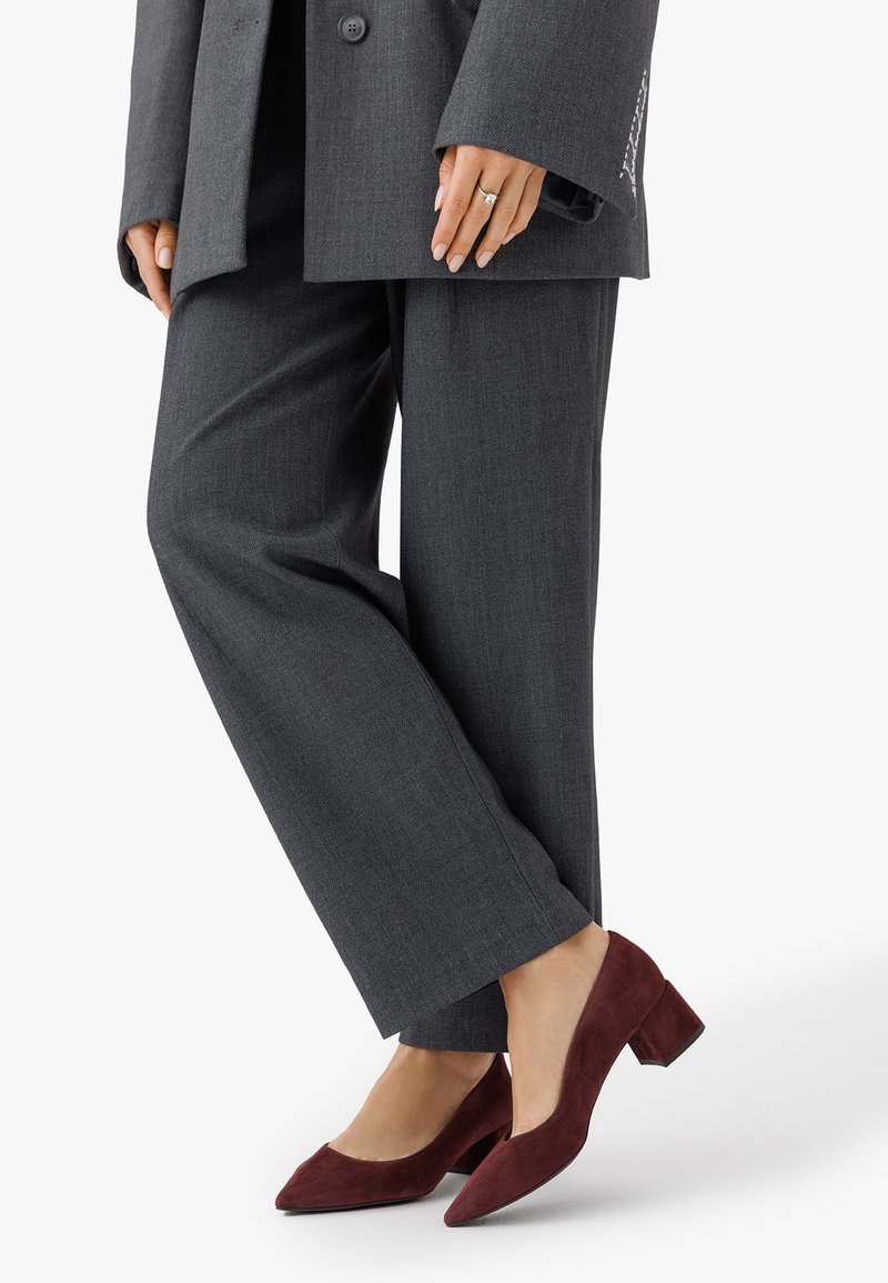 Sive prilagojene hlače v kombinaciji s burgundskimi semiš blok petami; podrobnosti vključujejo nizko izrezan sprednji del in gladko teksturo.