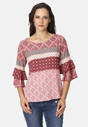 Blusa roja con estampado y mangas acampanadas, que presenta múltiples diseños textiles, incluyendo motivos geométricos y florales, en diferentes tonos de rojo y crema.