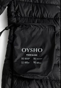 Črn napihnjen plašč z gladko, sijočo teksturo. Ima velik žep z belim besedilom, ki navaja 100 % perja, vodoodporno in odporen na veter.