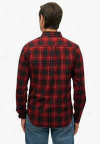 Rood en groen geruite knoopshirt met lange mouwen en kraag, met een rechte zoom en witte stikdetails.