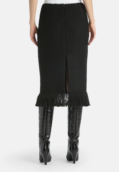 Black knitted skirt with a textured surface, featuring a fringe hem and back slit. Paired with high, glossy black heeled boots.