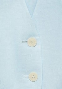 Tissu bleu clair texturé avec deux boutons ronds écru cousus verticalement sur un vêtement.