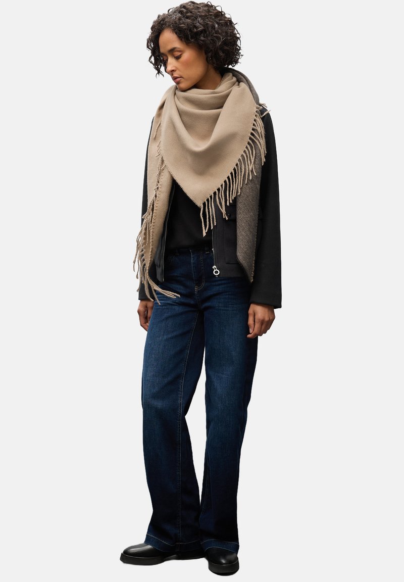 Beige uldscarf med frynser, båret over en sort top og grå overtøj, parret med mørkeblå jeans og sorte ankelstøvler.