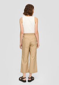 Beige, wijde broek van lichtgewicht stof met een elastische tailleband en twee achterzakken, gecombineerd met een witte mouwloze top.