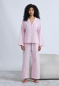 Σετ ρόμπας με ροζ καρό μοτίβο που περιλαμβάνει πουκάμισο με κουμπιά και μακριά μανίκια, καθώς και παντελόνι με φαρδιά πόδια, κατασκευασμένο από υφή υφάσματος.