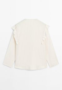 Crème lange mouwen blouse met ruches die van de schouder tot halverwege de mouw aan beide zijden lopen, tegen een witte achtergrond.