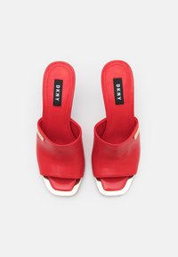 Des sandales à glissière en cuir rouge avec un bout ouvert et un talon carré. Présentent un accent doré et le logo DKNY sur la sangle. Texture lisse.