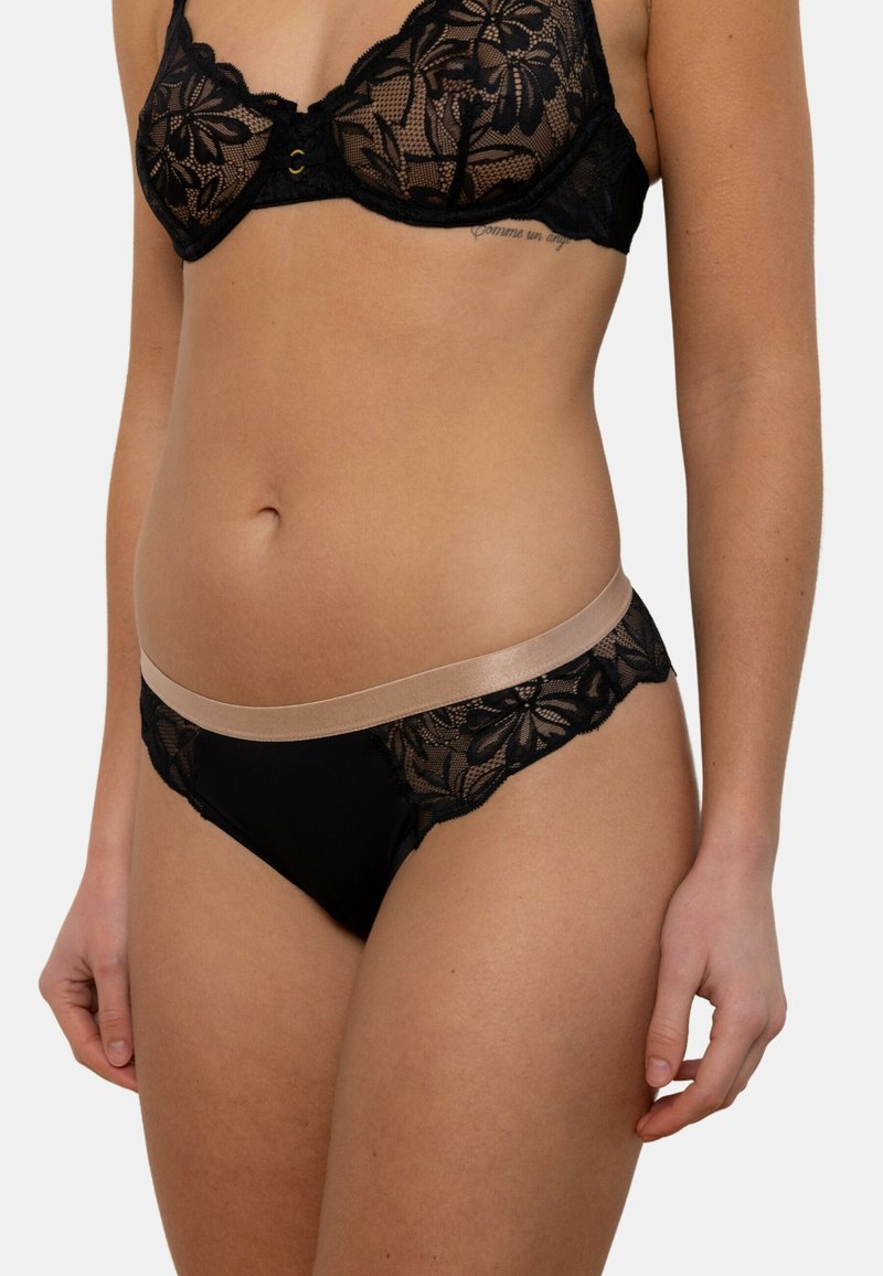 Soutien-gorge en dentelle noire avec motif floral et une ceinture en satin beige, présentant une conception structurée et un soutien par armature.