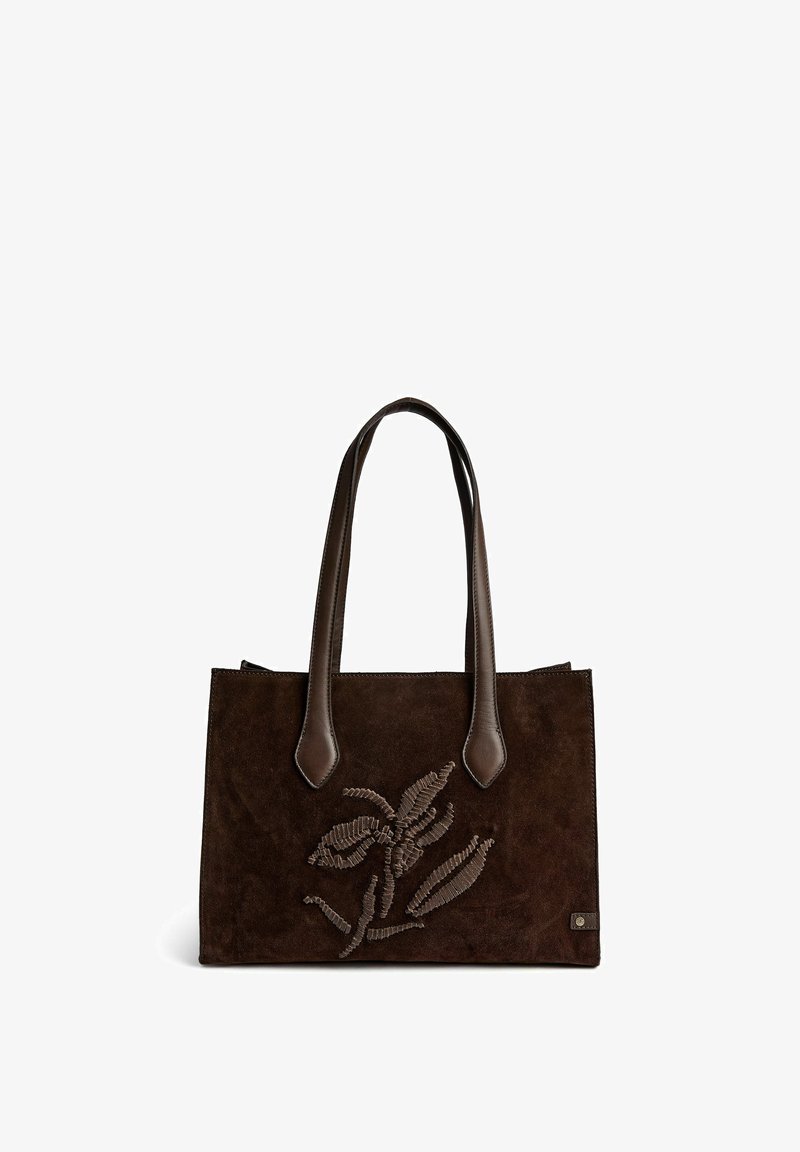 Sac à main en daim marron foncé avec deux poignées en cuir et un motif de feuille cousu sur le devant, sur fond blanc.