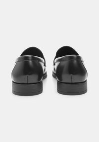 Mocassins en cuir noir avec une texture lisse, bout arrondi et détails de couture subtils. Semelle en caoutchouc noire plate et solide. Design global minimaliste.