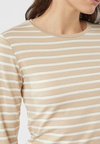 Beżowa koszula z długim rękawem, ozdobiona poziomymi białymi paskami, z okrągłym dekoltem i miękką fakturą, z dopasowanymi rękawami i gładkim wykończeniem.