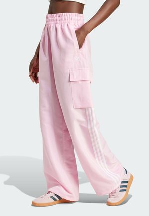 Person iført løse lyserøde cargobukser med elastik i taljen og hvide striber, kombineret med lyserøde Adidas-sneakers med gummisåler.