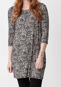 Černý a krémový tunikový top s paisley vzorem, tříčtvrtečními rukávy a zakulaceným lemem, vyrobený z měkkého materiálu. Nosený s černými legínami.