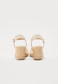 Zapatos de espadrilles beige con una suela media de yute trenzado, una correa para el tobillo de tela texturizada y un pequeño detalle de hebilla dorada.