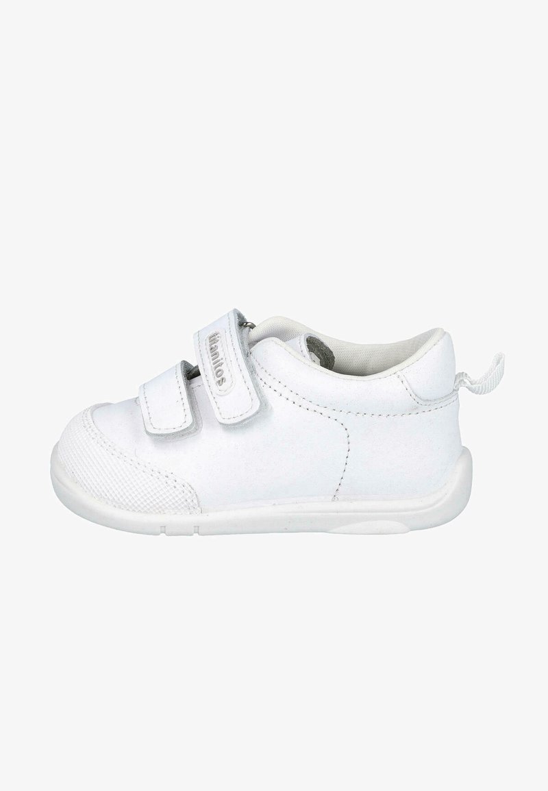 Zapatilla blanca con dos correas de velcro, parte superior de sintético liso, puntera texturizada y suela de goma. Forma redondeada con una pestaña en la parte posterior.