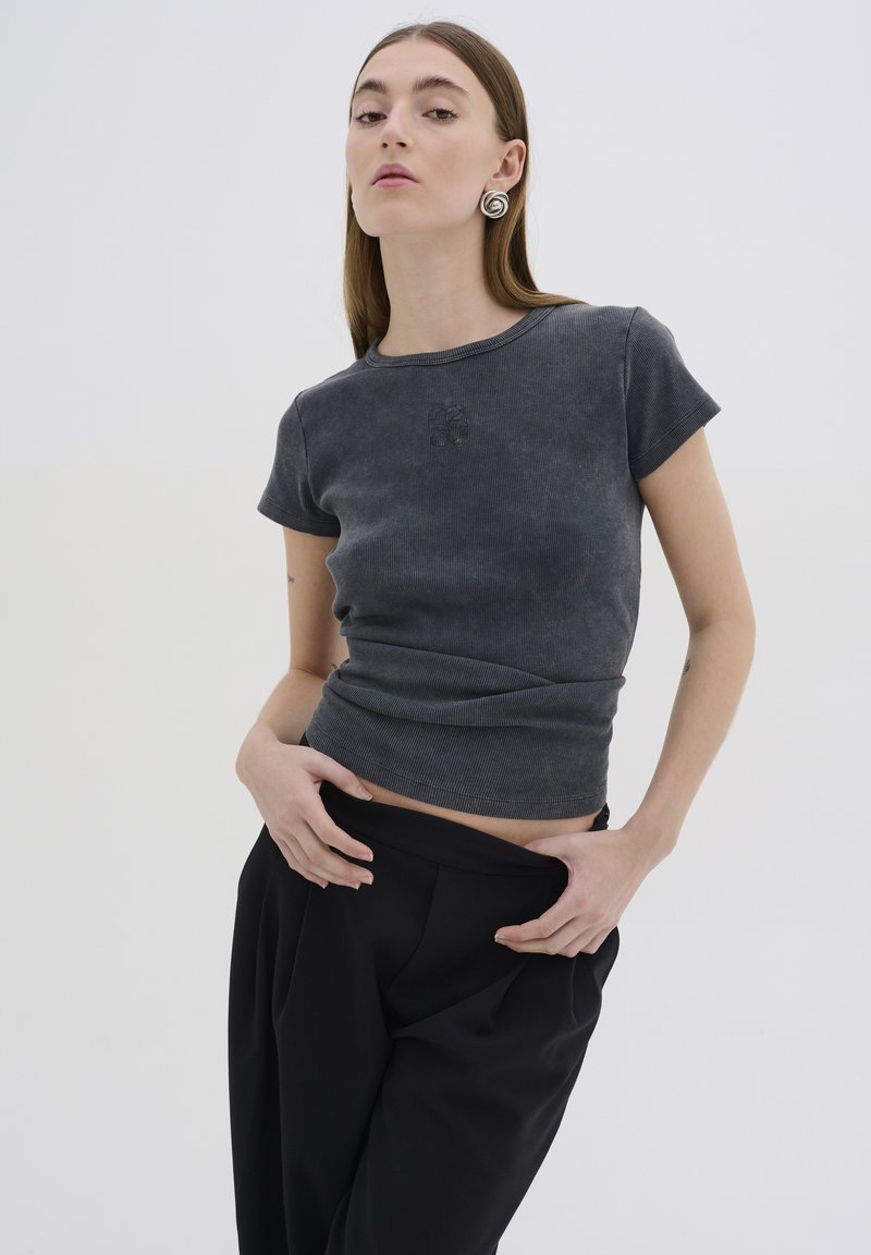 Top grigio a maniche corte con righe e design aderente, caratterizzato da un sottile logo ricamato sul petto, abbinato a pantaloni neri larghi.