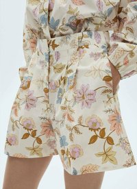 Floral-patterned shorts in cream fabric featuring pastel pink, blue, and gold flowers. Includes pleats and side pockets for added detail.
