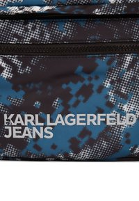 Blau- und schwarz strukturierter Stoff mit einem Camouflage-Muster. Das "Karl Lagerfeld Jeans"-Logo in fettem Grau am unteren Rand mit einer Reißverschlusstasche.