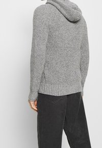 Grå stickad hoodie med ett strukturerat mönster, med en smal midja och långa ärmar. Matchad med svarta kordbyxor.