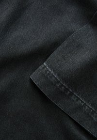 Svart denimtyg med en slät textur, med en vikt kant och synlig söm, delvis belyst för att framhäva ytan.