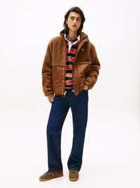 Veste en polaire marron et en nylon avec fermeture éclair à l'avant, superposée à un polo rayé. Porte avec un jean bleu et des baskets marron. Texture lisse dans l'ensemble.
