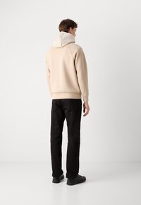Sweat-shirt à capuche beige avec une capuche de couleur claire, associé à un pantalon noir et des chaussures noires. Texture lisse et design décontracté.
