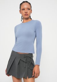 Jasnoniebieski top z długim rękawem i okrągłym dekoltem, zestawiony z szaro-plisowaną spódnicą z przodem wiązanym. Gładka tekstura materiału.