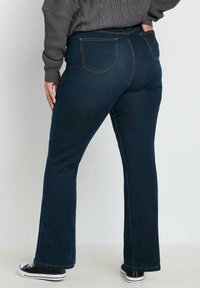 Vidgade mörkblå jeans har fem fickor, kontrasterande guldstickningar och en något strukturerad midjeband, i kombination med svarta sneakers.