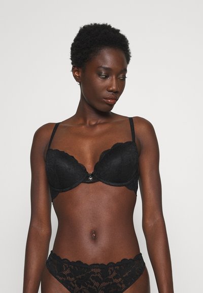 Soutien-gorge en dentelle noire avec bonnets moulés, bretelles réglables et un détail décoratif central. Accompagné d'un string en dentelle assorti avec des bords festonnés.