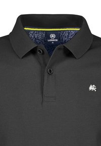 Czarna koszulka polo z teksturowanej tkaniny, z zapięciem na dwa guziki i srebrnym logo. Posiada wzorzystą wewnętrzną kołnierz z żółtym akcentem.