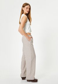 Top corto blanco sin mangas y pantalones de pierna ancha a rayas de talle alto en tonos beige y marrón, con bolsillos laterales y un ajuste relajado. Tacones gruesos marrones.