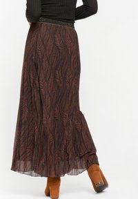 Maxikjol i mörk tyg med ett lövmönster i rostfärg. Har en strukturerad svart midja med en aning lyster. Bärs med bruna klackstövlar.