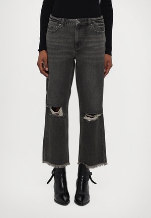 Jeans neri a vita alta con tagli strappati alle ginocchia, orlo sfilacciato e design classico a cinque tasche, abbinati a stivaletti neri alla caviglia.
