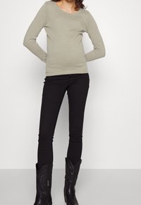 Haut à manches longues texturé vert clair, col rond, associé à un jean skinny noir et des bottes de cowboy noires hauteur genou avec des coutures décoratives.