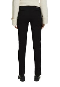 Svarta tapered byxor i slät tyg, med två bakfickor och midjehöjd, tillsammans med svarta skor och en ljus färgad tröja.