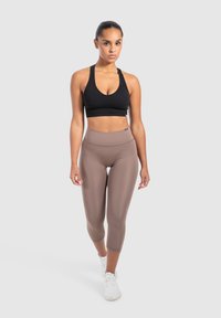 Un reggiseno sportivo nero e leggings a vita alta marroni, design aderente, texture liscia, con un logo bianco sulla vita, abbinati a sneakers bianche.