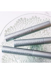 Drie zilveren mascara-tubes gelabeled "Better Than Sex" met textuur en waterdruppels, tentoongesteld op een glazen schaal met structuur.