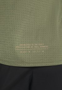 Grön sporttröja i texturerad taft med små perforeringar, guldtryck med specifikationer och rak nederkant.