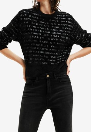 Pull noir en peluche avec des motifs de texte en blanc. Manches longues et encolure ras du cou, associé à un jean noir taille haute.