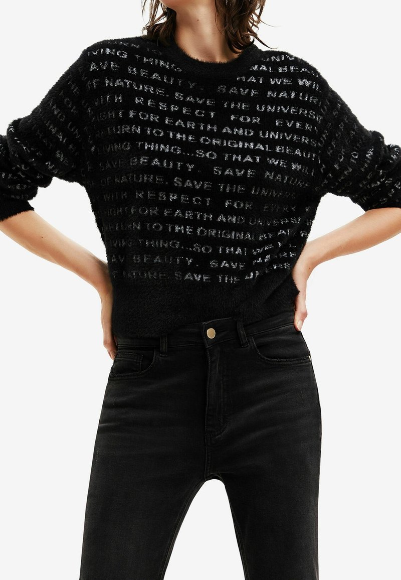 Czarny puszysty sweter z białymi wzorami tekstowymi. Długie rękawy i okrągły dekolt w połączeniu z czarnymi dżinsami o wysokim stanie.
