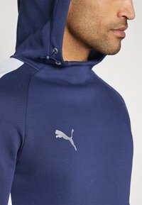 Navy capuchon sweatshirt met een gestructureerde afwerking, met witte schouderaccenten en een reflecterende zilveren Puma-logo op de borst.