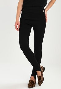 Svarta leggings med ett slätt tyg och två guldzippade fickor, ihop med leopardmönstrade ballerina-skor med rund tå och låg klack.