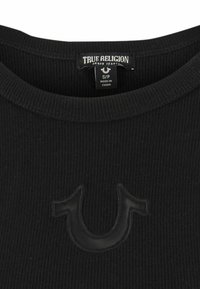 Chemise en tricot côtelé noir avec un col rond, présentant un logo True Religion ton sur ton à l'avant et une étiquette d'entretien à l'intérieur du col.