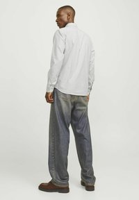 Biała koszula z długim rękawem w pionowe szare paski, zestawiona z luźnymi niebieskimi dżinsami. Ciemnobrązowe buty dopełniają stylizację.