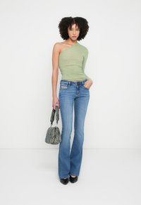 Roheline ühe õlaga topp, keha järgnev lõige; helerohelised põskniidipüksid; tekstuurse halli käekott; läikivad mustad kõrged kontsad. Sile kangas ja kohandatud istuvus.