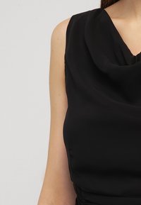 Vestido negro sin mangas con un escote drapeado, fabricado en una tela suave. Presenta una silueta ajustada con un sutil fruncido en la cintura.