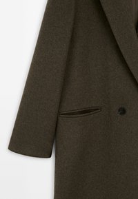 Manteau en laine olive foncé avec manches longues, un bouton noir unique et une poche fendue horizontale sur le devant.