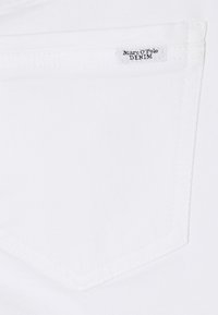 Tissu en denim blanc avec une poche cousue portant une étiquette avec l'inscription "Marc O'Polo DENIM." Texture lisse et design simple.