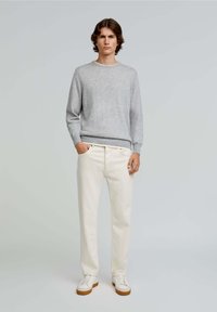 Pulover gri tricotat cu guler rotund, asortat cu pantaloni de culoare crem și adidași albi cu talpă maro. Design simplu, clasic.